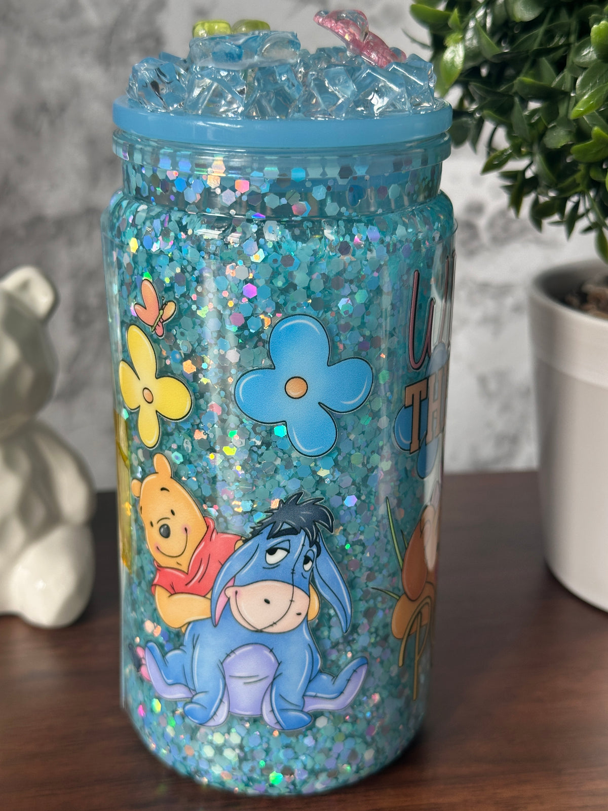 Image 3 (side - Pooh y Eeyore): "Dreamy Blue Glitter Tumbler side view — Pooh and Eeyore among flowers sublimation design on blue glitter tumbler, handcrafted at Motiva Ink Studio"