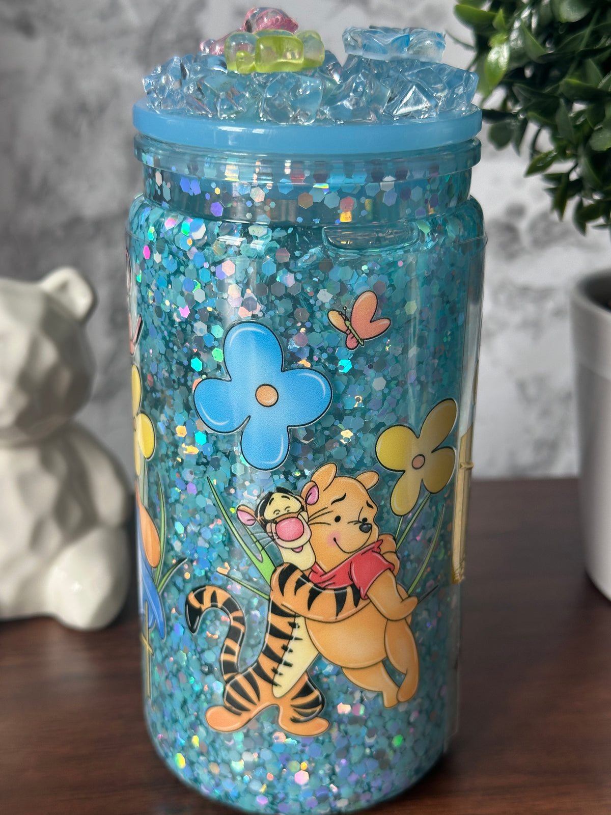 Image 2 (side - Tigger y Pooh): "Dreamy Blue Glitter Tumbler side view — Tigger and Pooh among flowers sublimation design on blue glitter tumbler, handcrafted at Motiva Ink Studio"


